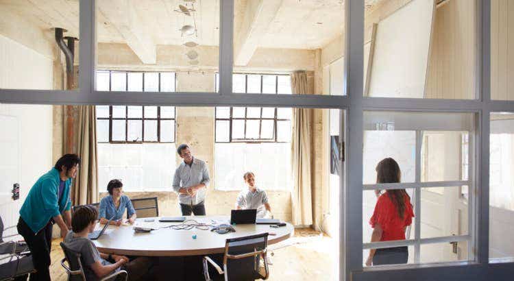 Group of six individuals in a well-lit modern conference room with large windows and exposed wooden beams.