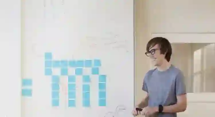 Smiling person presenting in front of a whiteboard with blue sticky notes, sketches, and system design notes