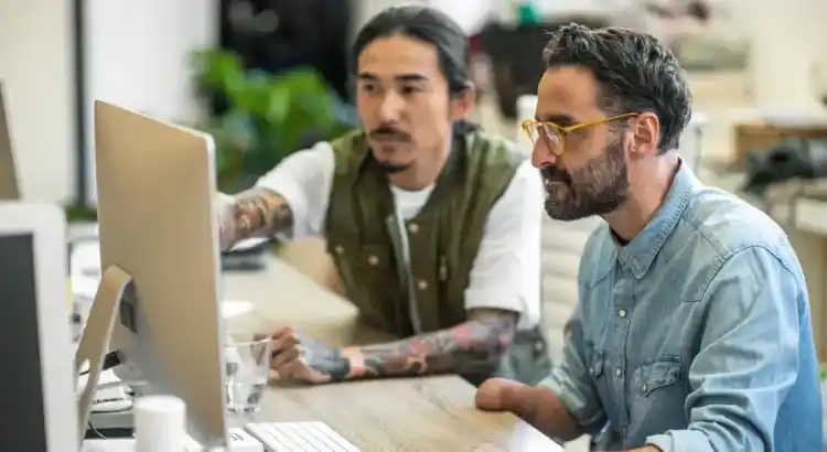 Two people working together at a desk in a modern office, pointing at a computer screen during discussion.