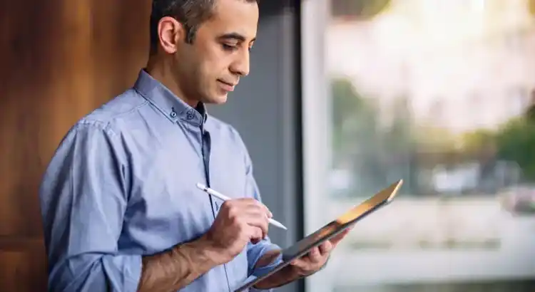 Person using a stylus on a tablet near a window in a modern indoor setting.