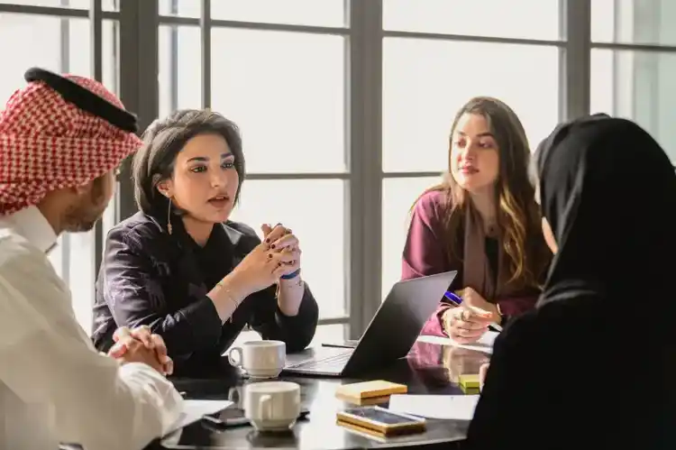 A picture of four people in a meeting with laptop and coffee mugs on the table
