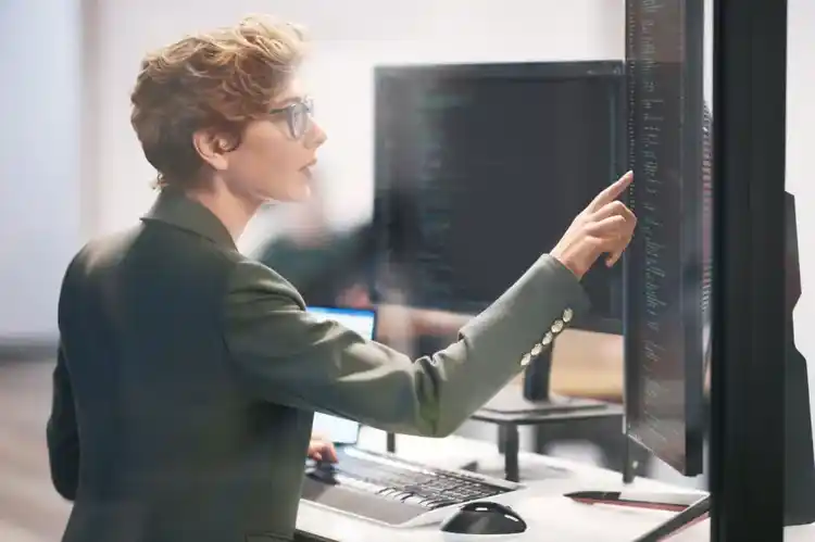 A picture of a woman working on a touch screen and a laptop