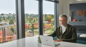 a man sitting at a table using a laptop in front of a window