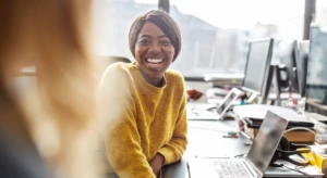 a woman sitting at a table with a laptop and smiling at the camera