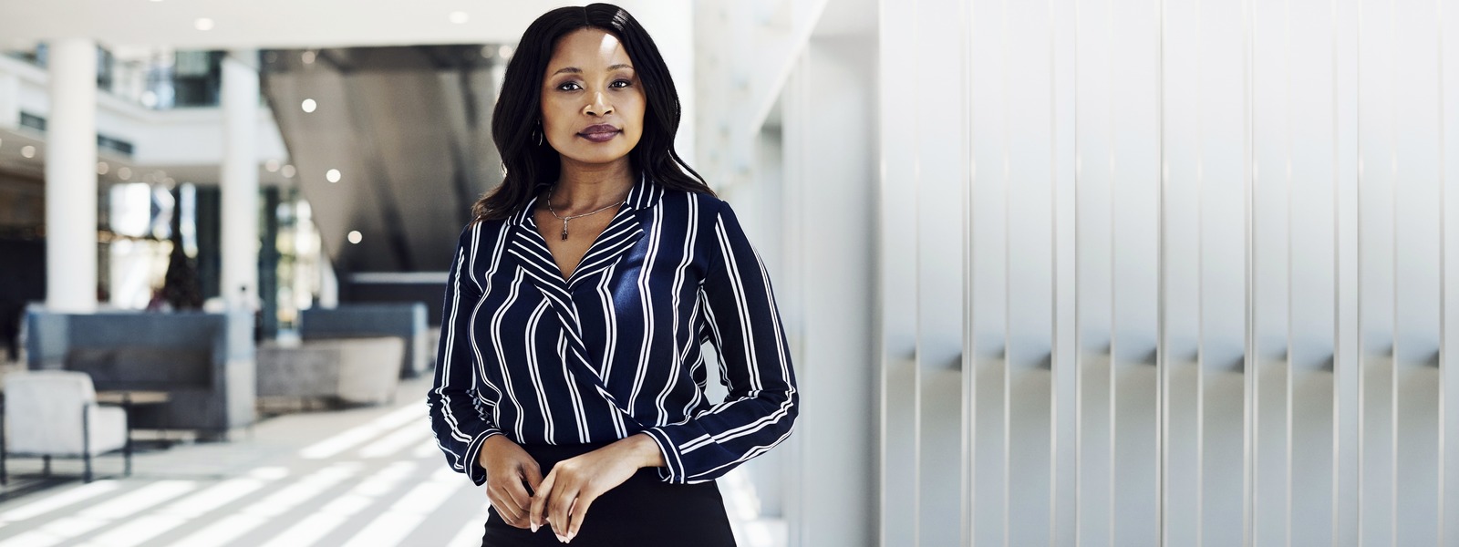 A Woman in a modern indoor space with navy blue and white striped blouse.