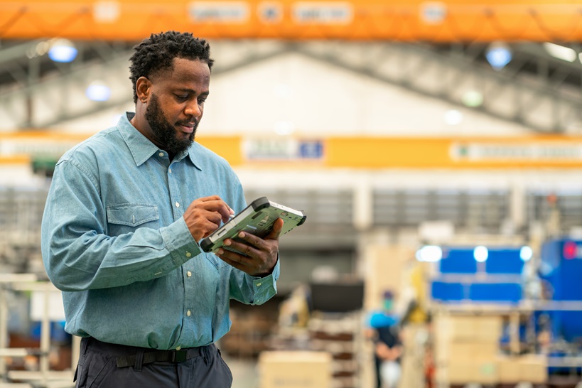 A manufacturing worker uses a tablet in a factory setting, illustrating Microsoft's support for digital transformation in industries and its focus on worker empowerment through technology.