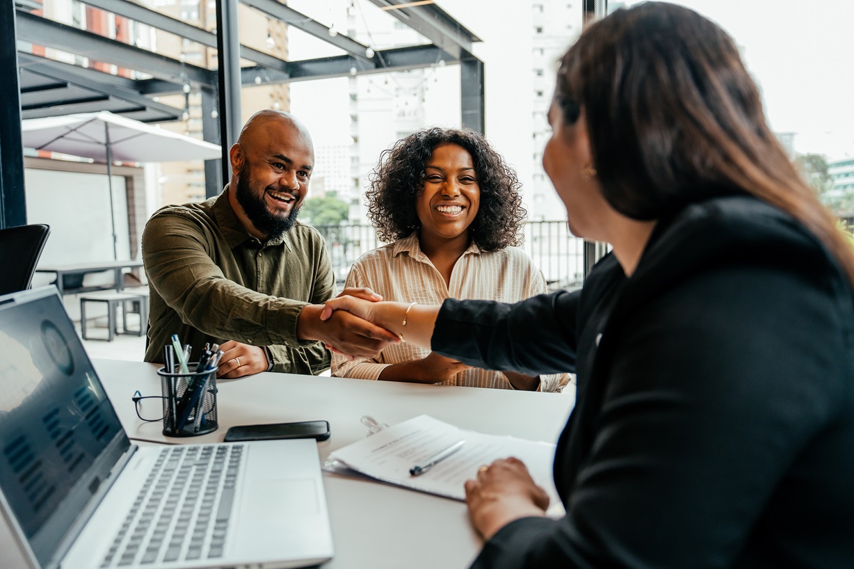 A Black couple shaking hands with a business professional across a table. it symbolizes partnership, agreement, and inclusivity in business negotiations.