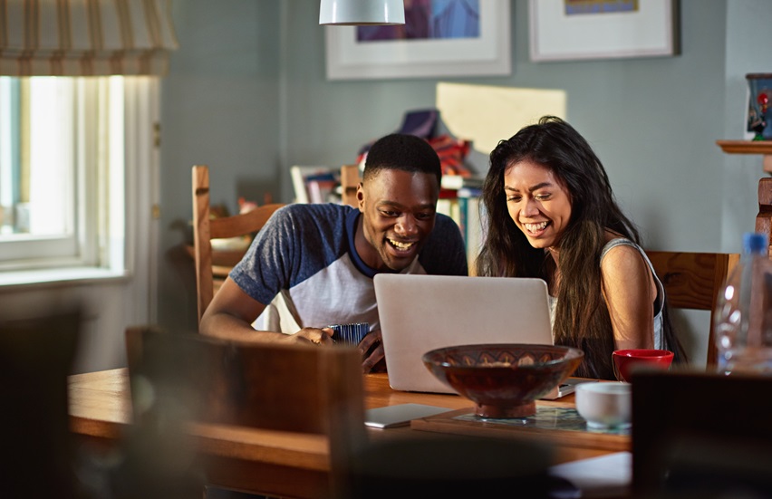 A man and a woman smiling while looking at laptop screen