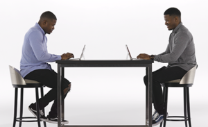 Image of twins sitting at a table, each with a laptop open.