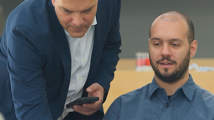 Two men are examining a cell phone together, appearing engaged in conversation.