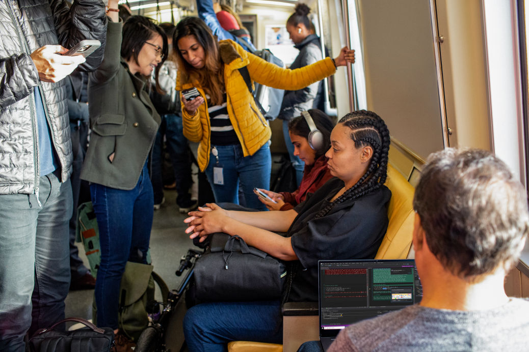 A group of people using their phones and laptops in the metro.