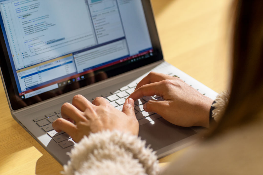 A person focused on typing on a laptop computer, with hands positioned on the keyboard.