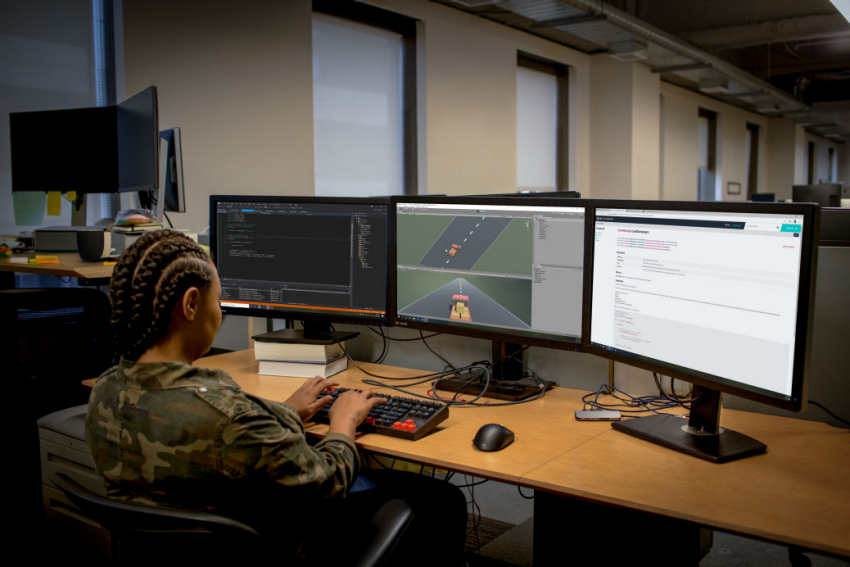 A woman seated at a desk, working on two computer monitors, focused on her tasks.