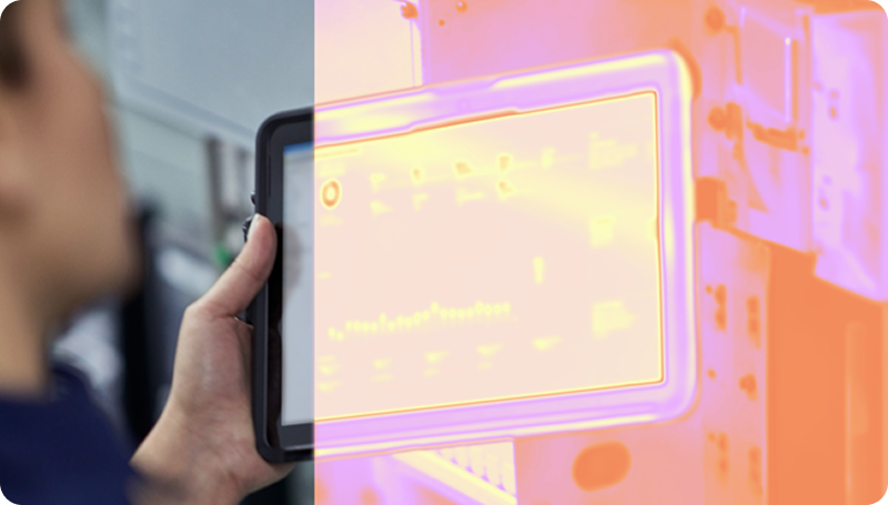 Blurred person holding a tablet near industrial equipment, with a pink‑orange overlay on the screen.