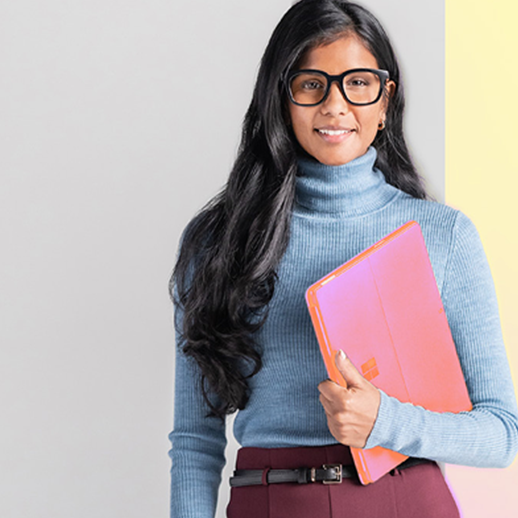 Young woman with glasses in front of a wall holding a laptop with her left hand