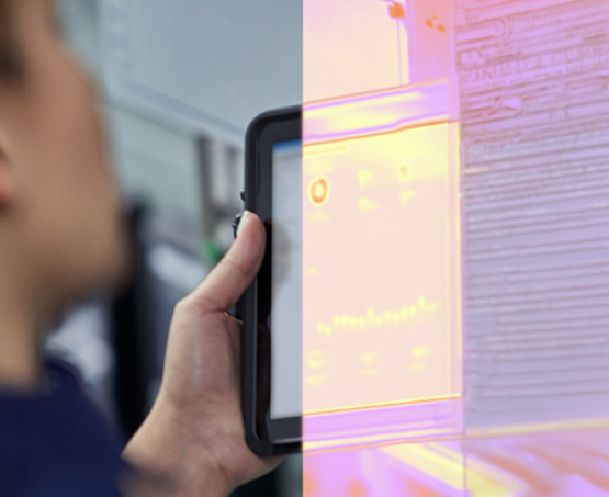 Blurred person holding a tablet near industrial equipment, with a pink‑orange overlay on the screen.