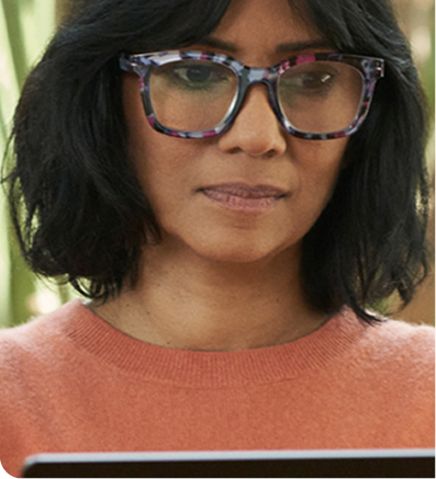 Person in an orange sweater working on a laptop indoors, with green plants in the background.