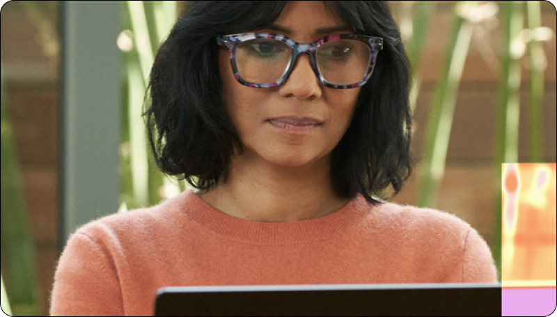 Person in an orange sweater working on a laptop indoors, with green plants in the background.