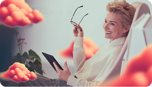 A woman holds glasses and a tablet in her hand and smiles relaxed.