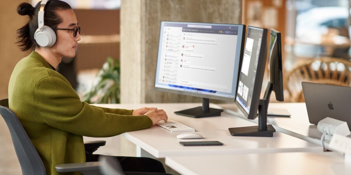 A man collaborating during a Microsoft Teams meeting while working in an open office setting on dual monitors.