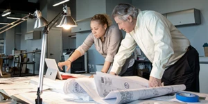 Dos personas mirando un dispositivo y papeles sobre la mesa