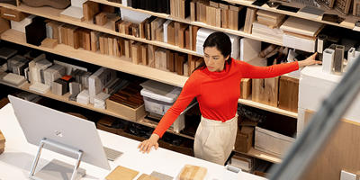 Mujer de pie frente a un estante de papel y mirando una computadora