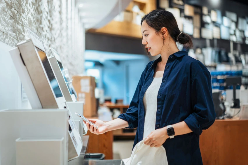 Young woman using contactless payment via her smartphone to pay at a self-checkout kiosk in the store. KEYWORDS: shopping; lifestyle; wireless technology; innovation; Hong Kong