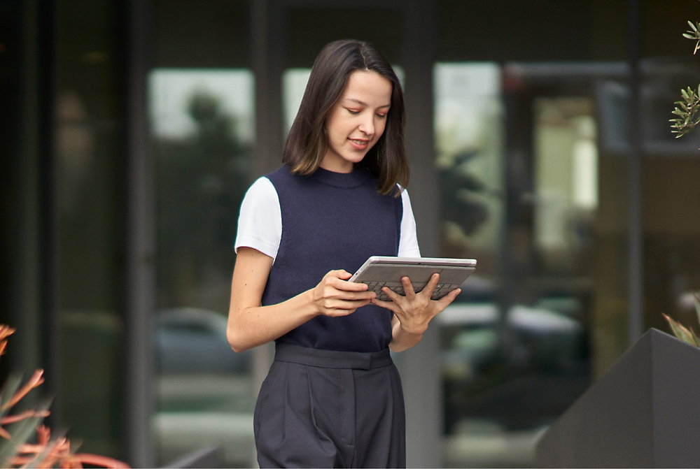 Une femme en costume d'affaires tient une tablette, paraissant professionnelle et engagée dans son travail.