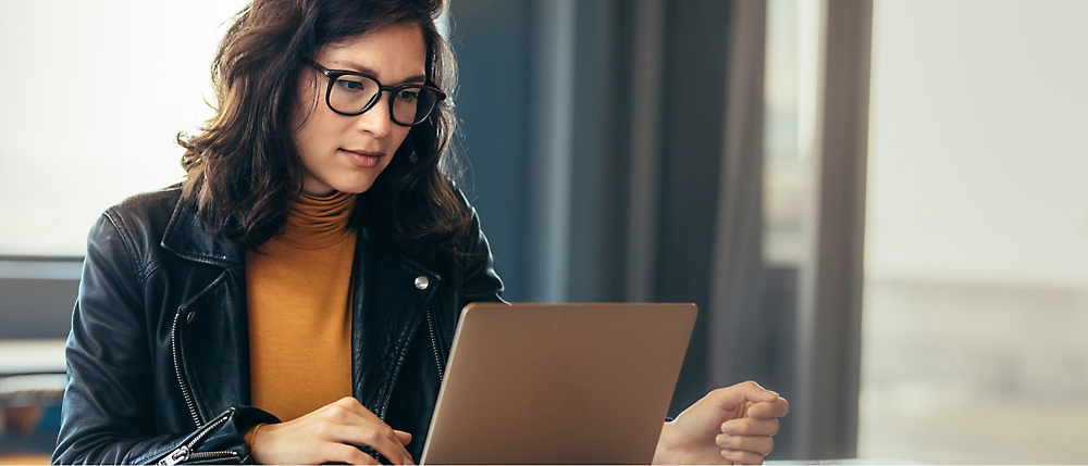 Une femme portant des lunettes est concentrée sur l'utilisation d'un ordinateur portable à un bureau.