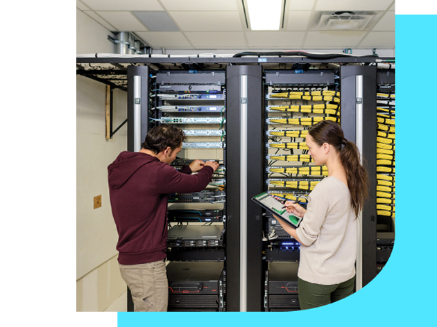 Seorang laki dan wanita dalam ruangan server sedang bekerja. sang wanita memegang tablet nya, dan si pria sedang memperbaiki server yang ada. 