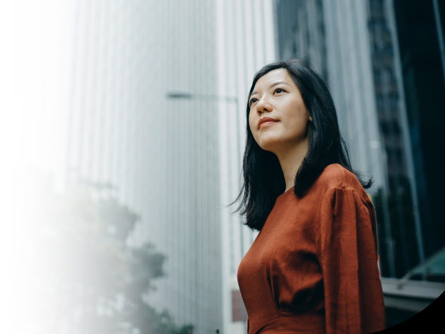 Seorang wanita yang sedang mengenakan pakaian kerja formal sedang mentap langit di luar kantor nya