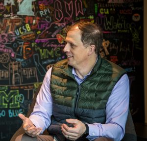 Jay Clem talks with a colleague in front of a chalk board. He is the leader of Core Services Engineering and Operations' Human Resource team.