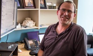 David Johnson sits at his desk smiling at the camera.
