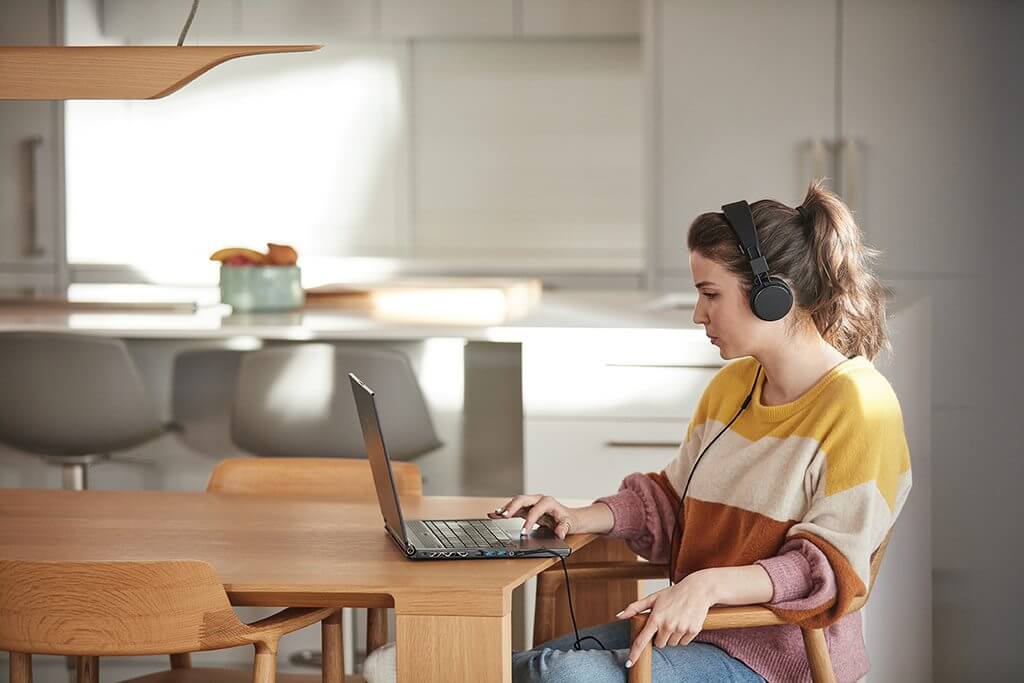 A woman sits at her kitchen table using Microsoft Teams to attend a meeting from home.