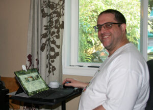 Carmichael Patton looks at the camera and smiles, and his laptop is in front of him.