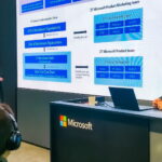 Carmichael Patton and Mark Skorupa stand on either side of a presentation slide of an overview of Microsoft’s Zero Trust security model.
