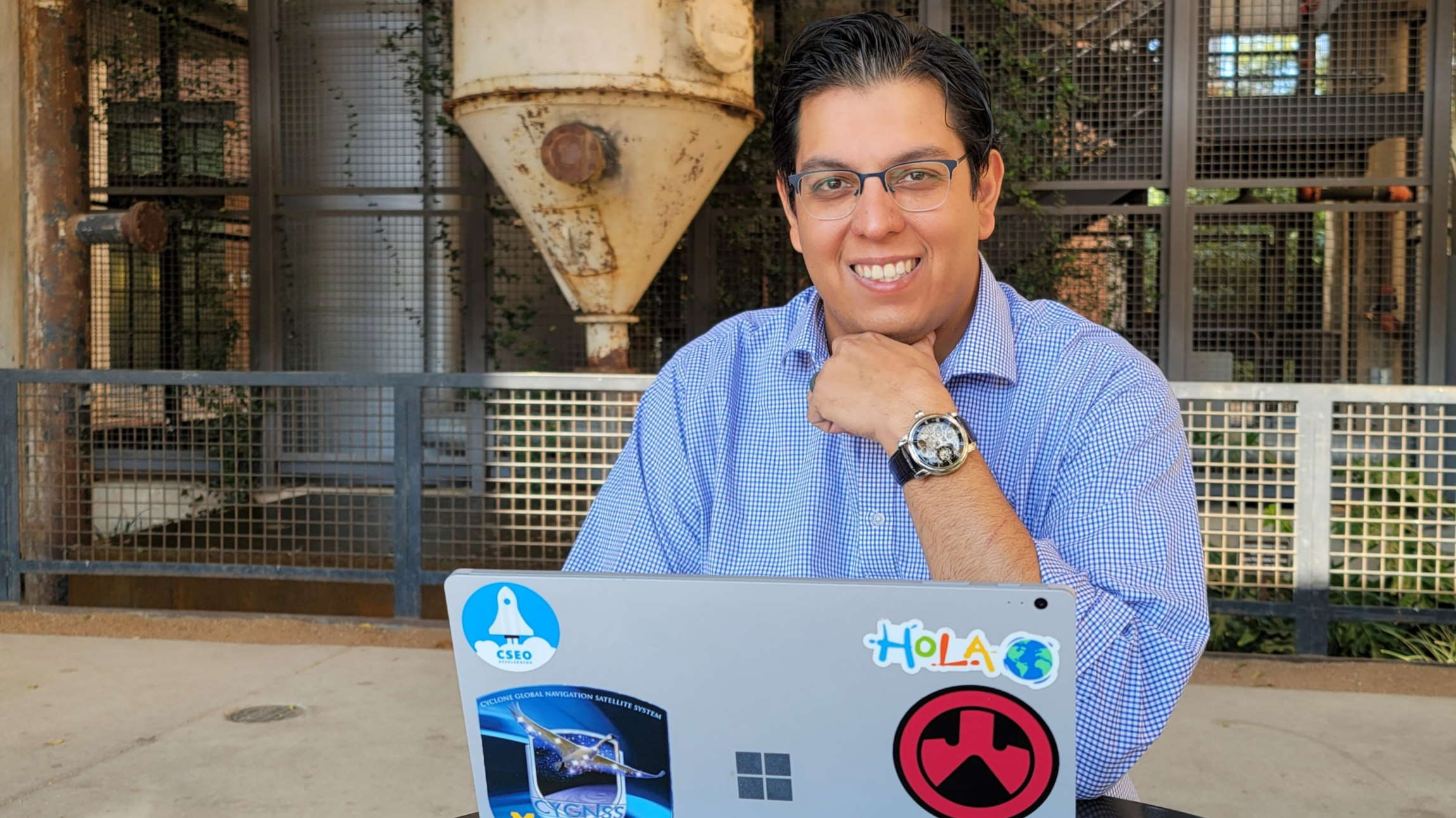 Paul Rojas sits at an outdoor table with his laptop and smiles at the camera.