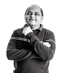 Manish Agrawal smiles as he stands looking at the camera with his arms folded. 