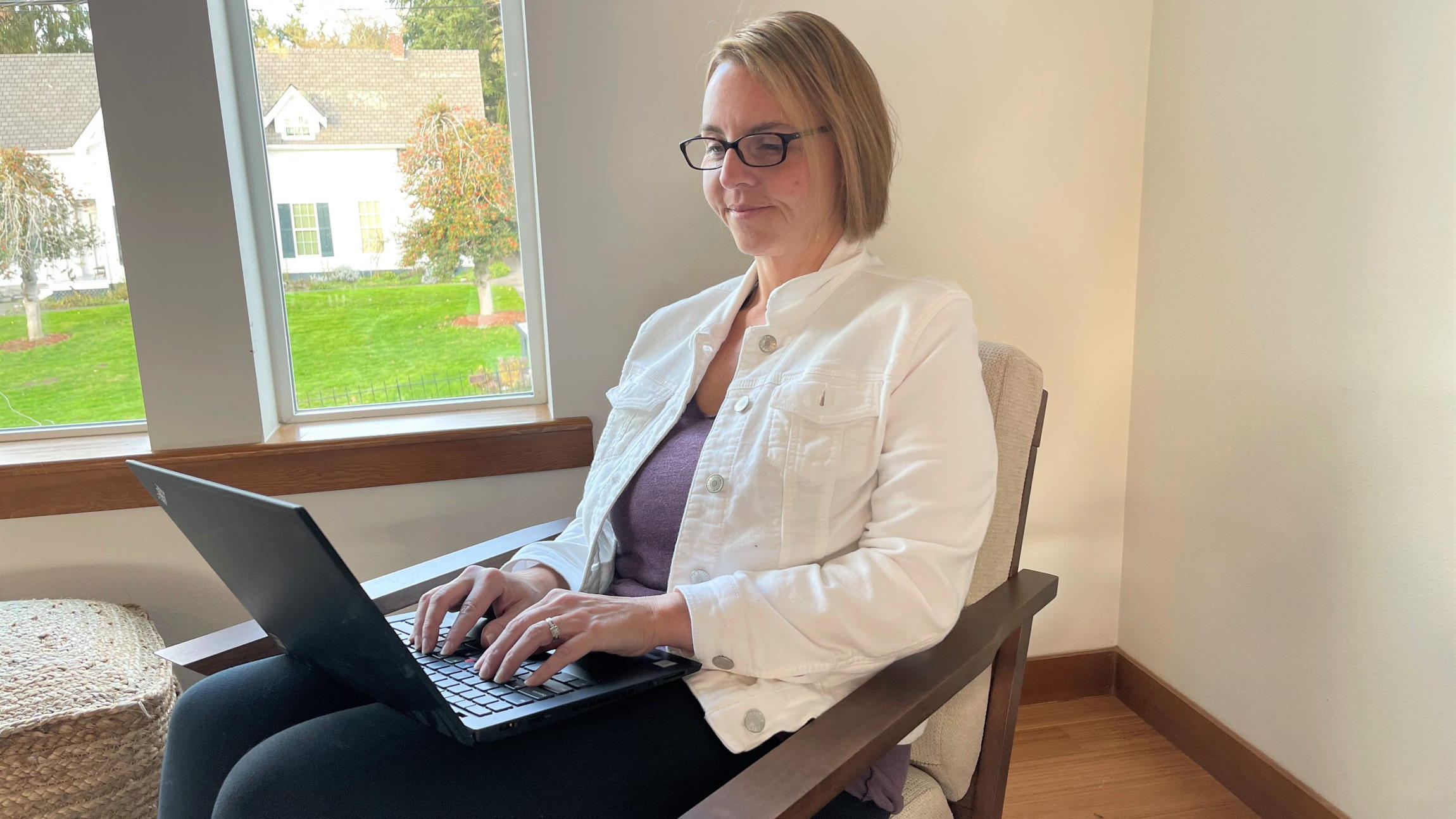 Dana Baxter sits by a window and works on her laptop computer.