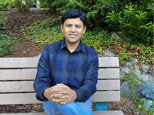 Prasad sits on a bench in front of a hedge outside of a Microsoft building.
