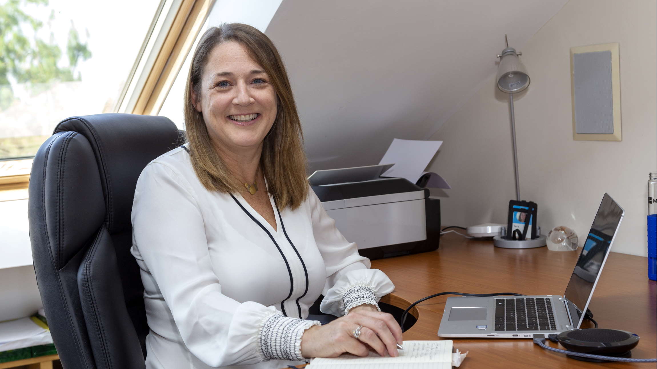 Tara Kelly sitting at a desk with laptop, smiling.