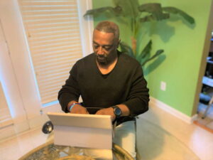 Reginald Albert sits at a tablte working on a laptop.