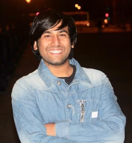 Singh, a wide smile on his face, stands with his arms crossed wearing a denim jacket.