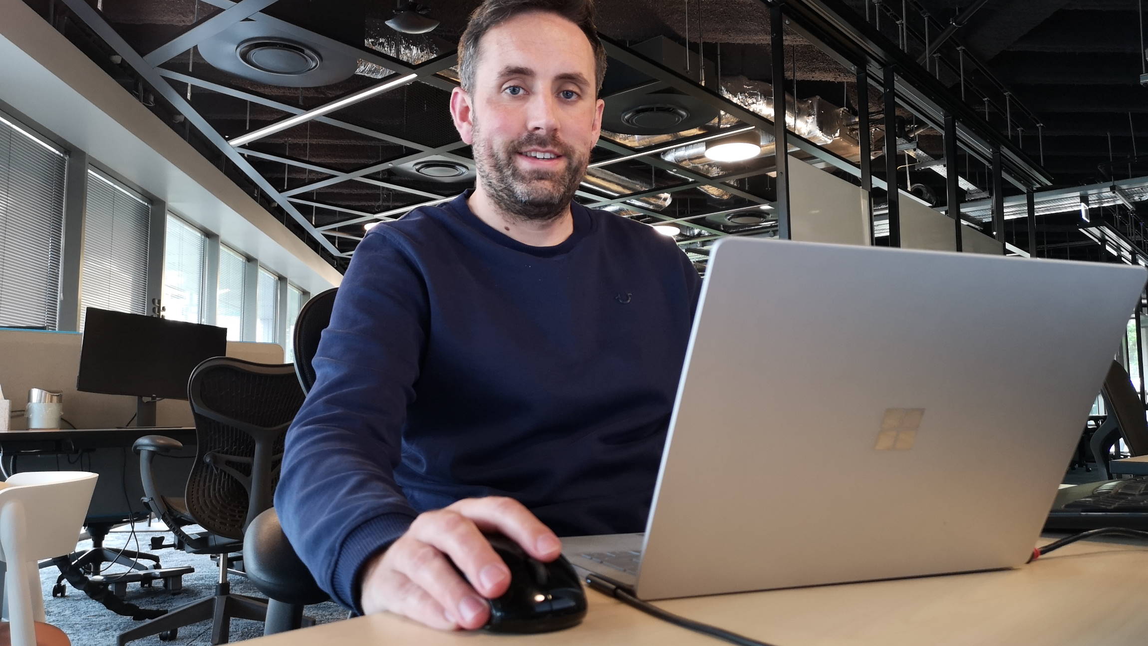 Paddy Colreavy, wearing a crewneck sweatshirt, works on a laptop in an empty office.
