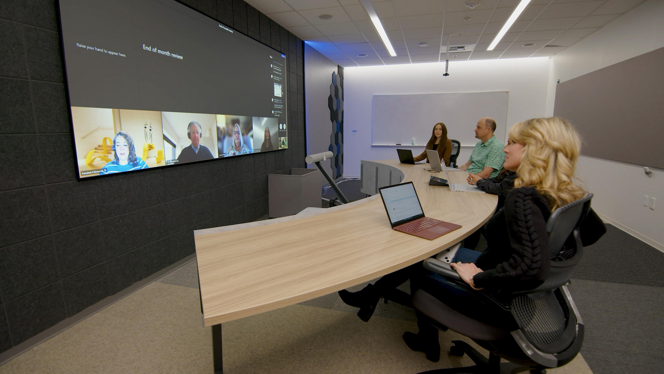 A Microsoft team meets at a curved desk facing a screen on the wall, allowing them to see everyone in the meeting equally.