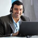 A Microsoft employee smiles as he attends a meeting virtually on his PC with his headset on.