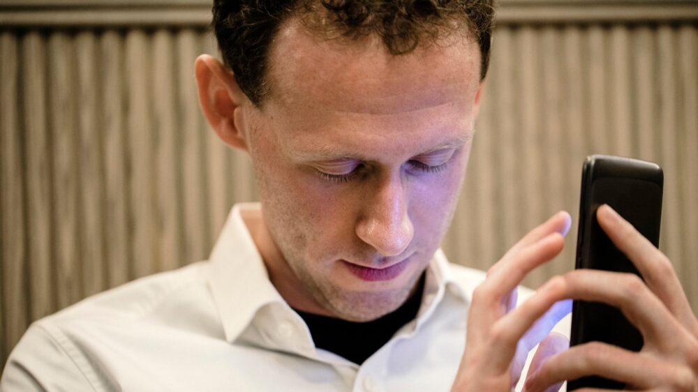 A close-up of a man with a smartphone in his hand. He is using an assistive mobile app for people with vision disabilities to assist him.