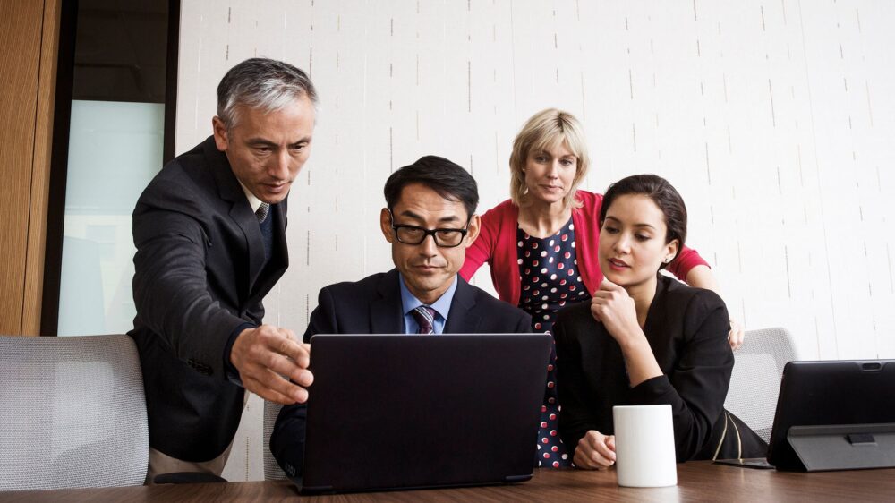 A group executives collaborate over a laptop.
