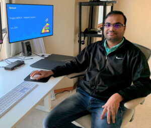 Chakri Thammineni sits next to his desk and smiles at the camera. His monitor reads “Project Natick– Network Solution.”