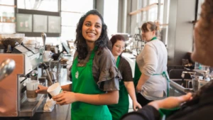 A Starbucks partner smiles at a customer while preparing coffee